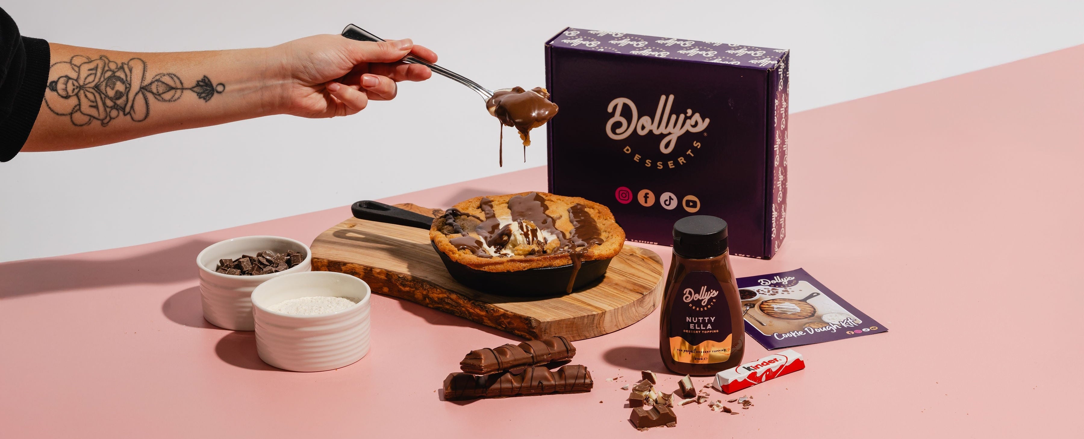 Person preparing a dessert with chocolate and a Dolly's box on a pink surface.